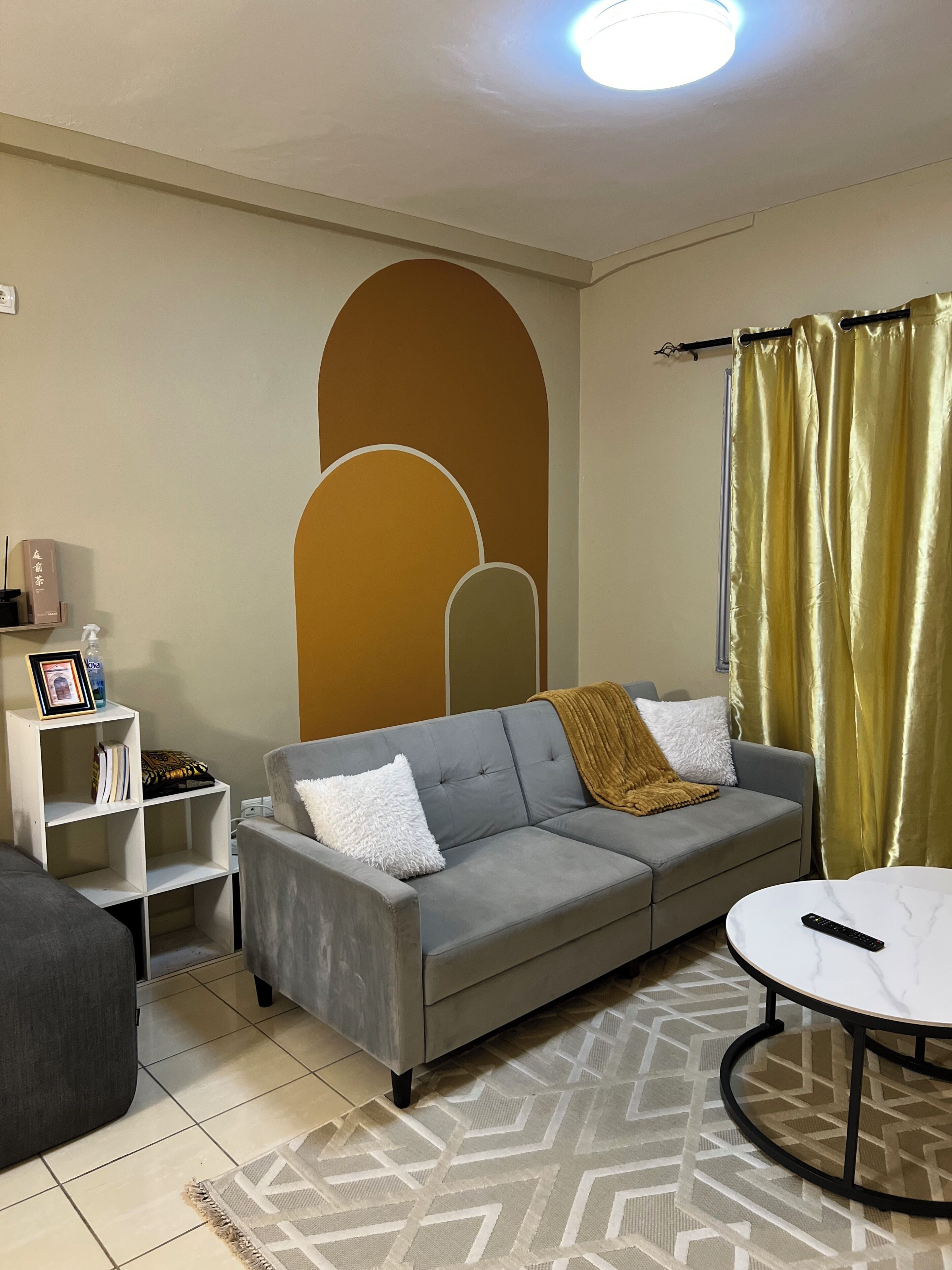 A living room with a grey sofa, a white coffee table, a patterned rug, and a bookshelf with books and a framed picture.