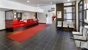 Een receptiegedeelte met een rode loper, een receptiebalie en een wachtruimte met stoelen.