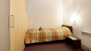 Een slaapkamer met een bed, een nachtkastje, een wandlamp en een deur.