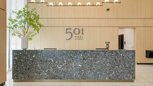 Vastaanottotiski, jossa on kyltti, jossa lukee ”501 First Residences”, ruukussa oleva kasvi ja moderni sisustus.