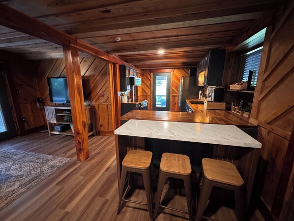 A wooden interior with a bar area, wooden flooring, and a television. - FUN! Log Cabin Hot Tub & Game Room w Pool Table Pets OK 3BR/2BA Sleeps 10 (Red Oak)