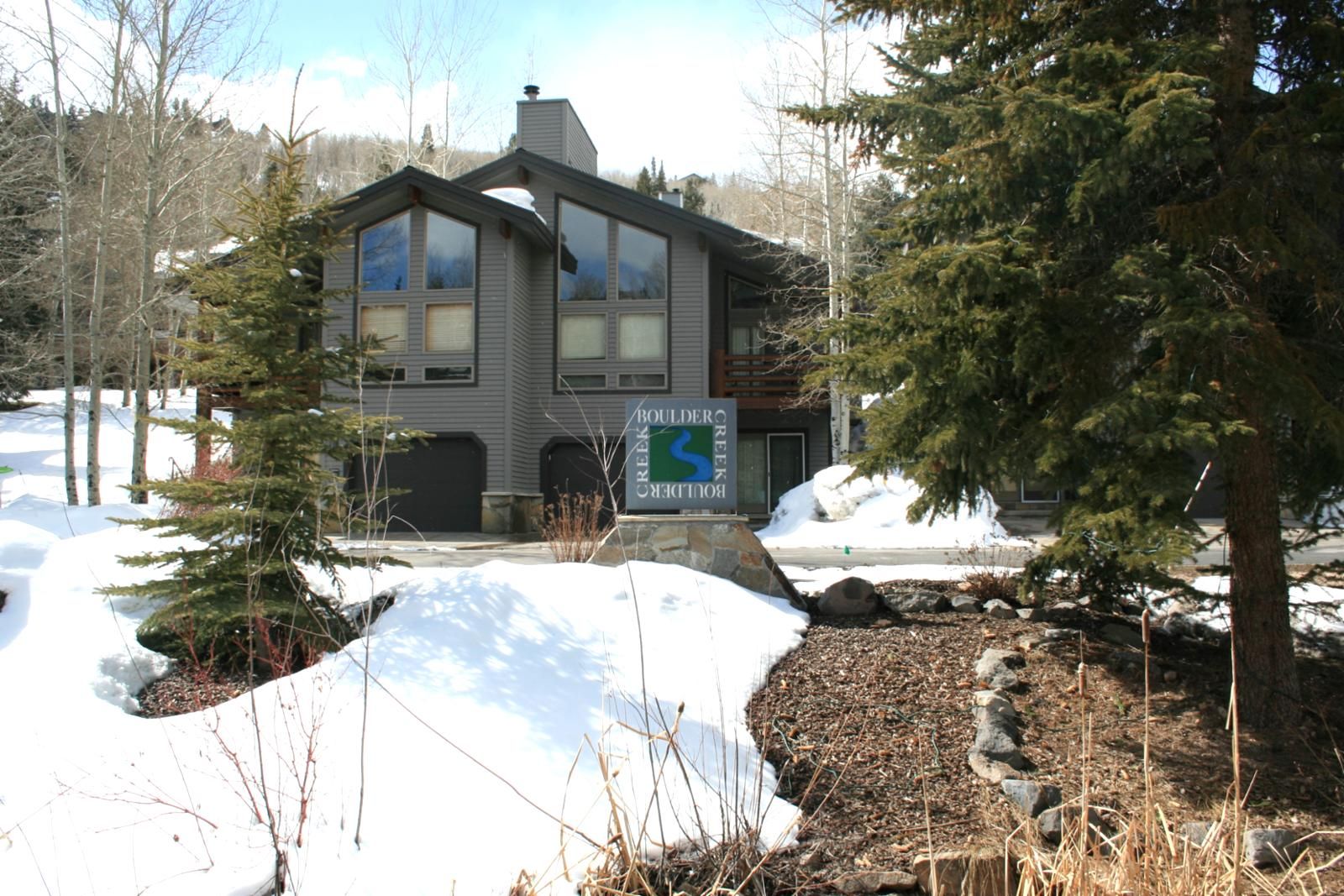 A modern two-story house with a stone foundation, large windows, and a sign indicating 'Boulder Creek'.