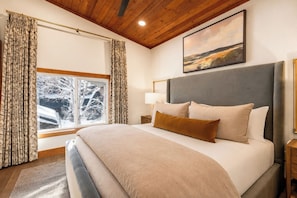Quarto com uma cama grande, cabeceira, mesa de cabeceira, abajur e janela com cortinas.