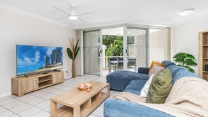 A living room with a TV, wooden coffee table, blue sofa, and a sliding glass door leading to an outdoor area. - Bliss On Beach Parade (Surfers Paradise)