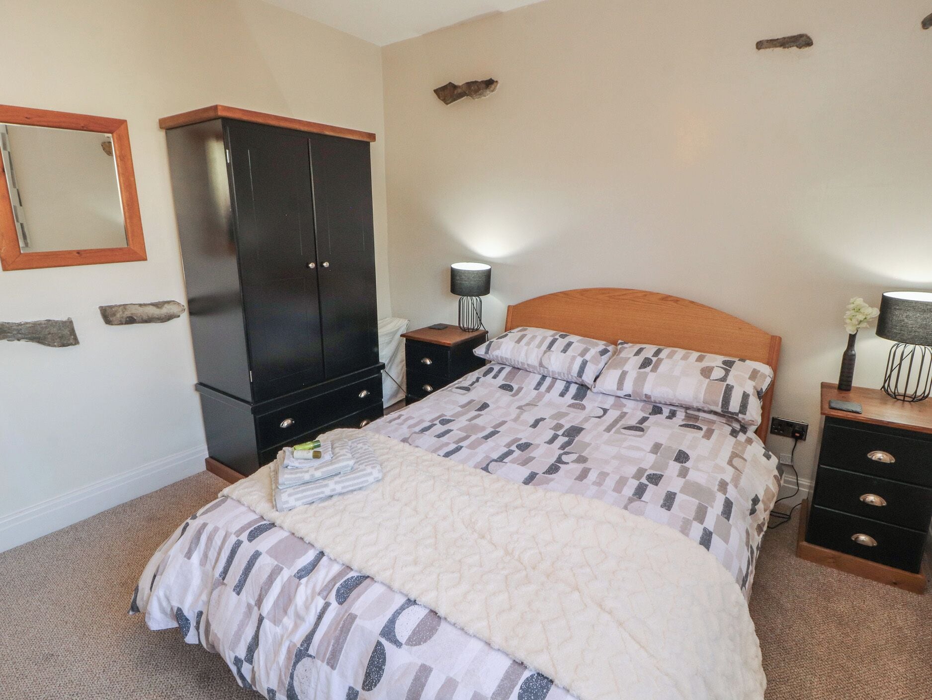 A bedroom with a bed, a wardrobe, a nightstand, a lamp, and a mirror.