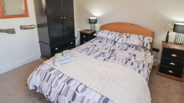 A bedroom with a bed, a wardrobe, a nightstand, a lamp, and a mirror. - Tullythwaite Barn (Kendal)