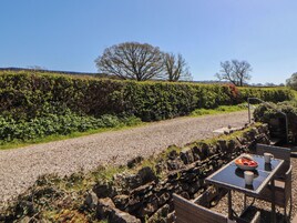 A gravel path with a stone wall and a table with a bowl of fruit and a cup.