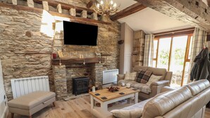 A stone-walled living room with a fireplace, leather sofas, a wooden coffee table, and a television mounted on the wall. - Tullythwaite Barn (Kendal)