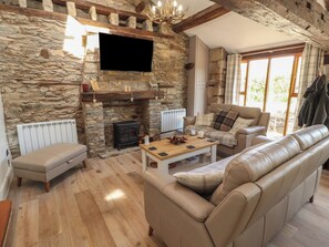 A stone-walled living room with a fireplace, leather sofas, a wooden coffee table, and a television mounted on the wall. - Tullythwaite Barn (Kendal)