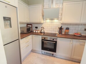 A modern kitchen with white cabinetry, a built-in microwave, a kettle, and a stove. - Tullythwaite Barn (Kendal)