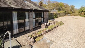 A rustic building with large windows, a gravel driveway, and a stone wall. - Tullythwaite Barn (Kendal)