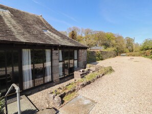 A rustic building with large windows, a gravel driveway, and a stone wall. - Tullythwaite Barn (Kendal)