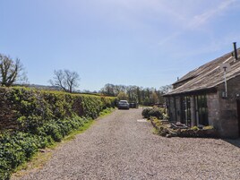 A gravel road leading to a stone building with a thatched roof, surrounded by greenery and trees.