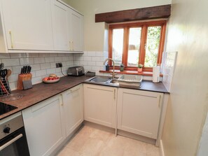 A compact kitchen with white cabinets, a countertop, a sink, a toaster, and a window with plants. - Tullythwaite Barn (Kendal)