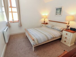 A bedroom with a bed, bedside tables, lamps, a radiator, a window with curtains, and a picture on the wall.