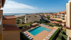Uma área de piscina com espreguiçadeiras, vista desobstruída da praia e um conjunto de edifícios residenciais.