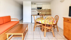 Um espaço de estar compacto com sofá, mesa de jantar, cadeiras, área de cozinha com micro-ondas e televisão.
