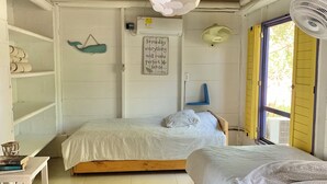 A bedroom with two beds, a white ceiling fan, a wall-mounted air conditioner, and a window with yellow shutters.