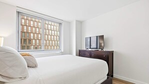 A bedroom with a bed, a TV on a dresser, and a window with a view of buildings. - Spacious Apt in Murray Hill (New York, NY)