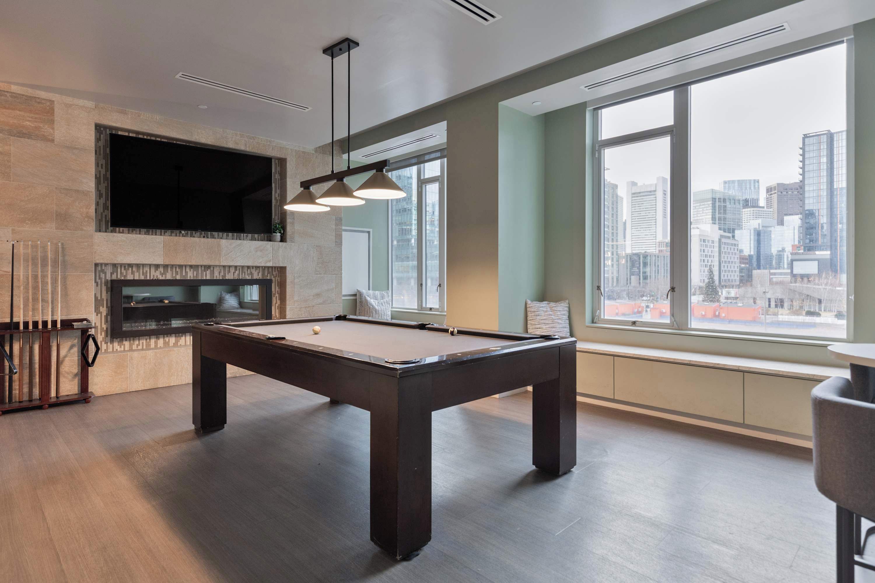Uma mesa de bilhar moderna em ambiente interno, vista para a cidade, lareira e uma janela grande.