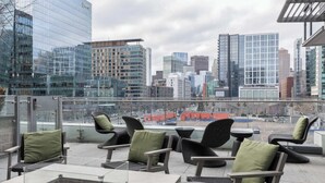 Una terraza en la azotea con mobiliario exterior, vistas panorámicas del horizonte urbano y arquitectura moderna.