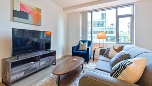 Een moderne woonkamer met een flatscreen televisie, een blauwe fauteuil, een grijze bank en een salontafel.