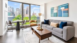 Una sala de estar moderna con un sofá gris, una mesa de centro y dos sillones. Hay ventanas amplias con vista a la ciudad.