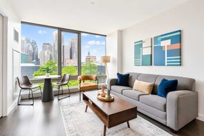 A modern living room with a grey sofa, a coffee table, and two chairs. There are large windows with a city view. - Lux Apt with Pool in Boston Seaport (Boston, MA)
