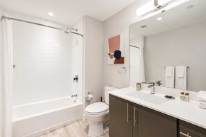 Un baño moderno con bañera, inodoro y tocador con espejo.
