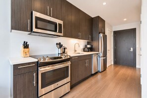 A modern kitchen with stainless steel appliances, wooden cabinets, and a white countertop. - Lux Apt with Pool in Boston Seaport (Boston, MA)