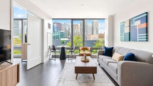 Una sala de estar moderna con sofá, mesa de centro y sillones, ventanas amplias con vista a la ciudad y obras de arte en la pared.
