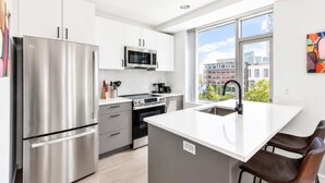 A modern kitchen with stainless steel appliances, a large window, and a view of buildings. - Luxury Apt On Canal in Cambridge (Cambridge, MA)