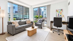 A modern office space with a grey sofa, a small round table, a black office chair, and a desk with a computer. - Luxury Apt On Canal in Cambridge (Cambridge, MA)
