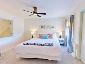 Ein Schlafzimmer mit einem Bett, Deckenventilator, Nachttischen und einem Fenster mit Vorhängen.