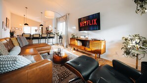 Una sala de estar moderna con un sofá de cuero, un sillón de cuero negro, un aparador de madera y un televisor grande que muestra 'NETFLIX'.