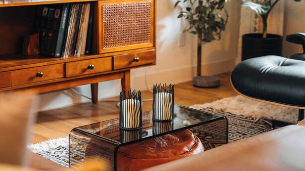 Una sala de estar con una mesa de centro de vidrio, un sofá de cuero, un aparador de madera con discos y una planta en maceta.