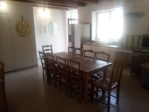Un coin repas avec une table et des chaises en bois, une cuisine équipée d’un réfrigérateur et d’un évier, et une fenêtre laissant entrer la lumière naturelle.