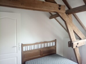 Une chambre avec une tête de lit en bois, une porte blanche et des poutres apparentes.