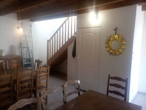 Un coin repas avec des meubles en bois, un escalier, une porte blanche et un miroir en forme de soleil.