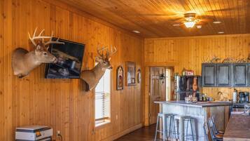 A cabin interior with wooden walls, mounted deer heads, a bar area, and a kitchen with modern appliances.