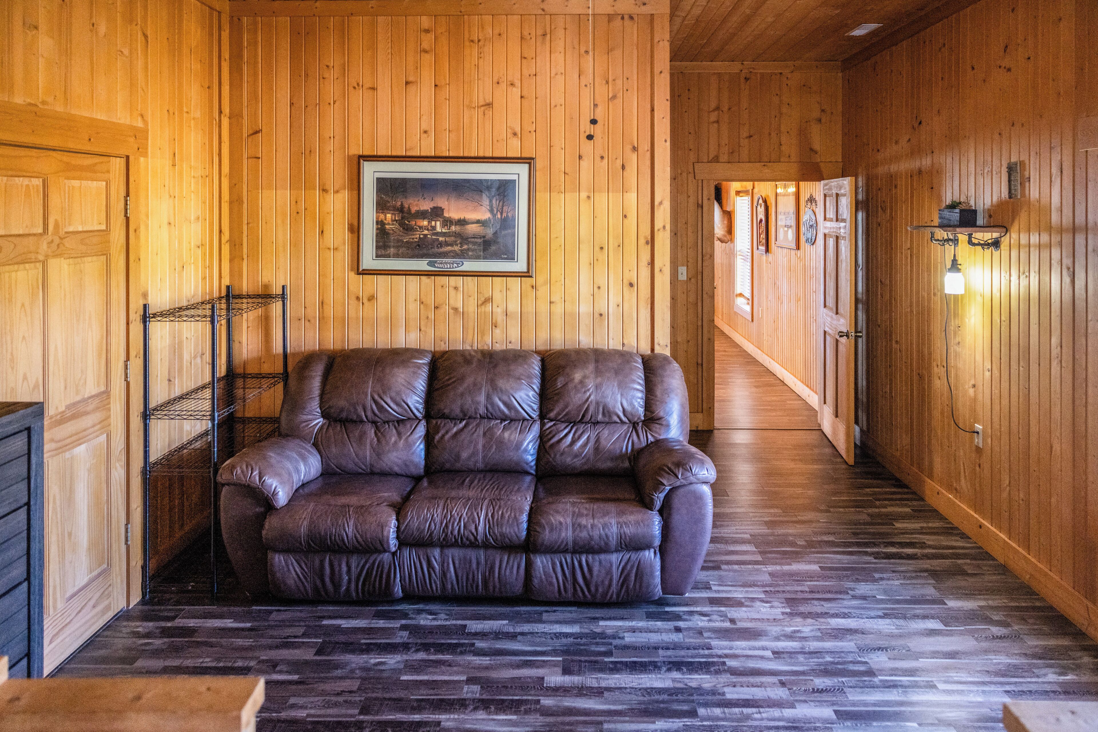 A wooden-paneled room with a leather sofa, a framed picture on the wall, and a hallway leading to other rooms.