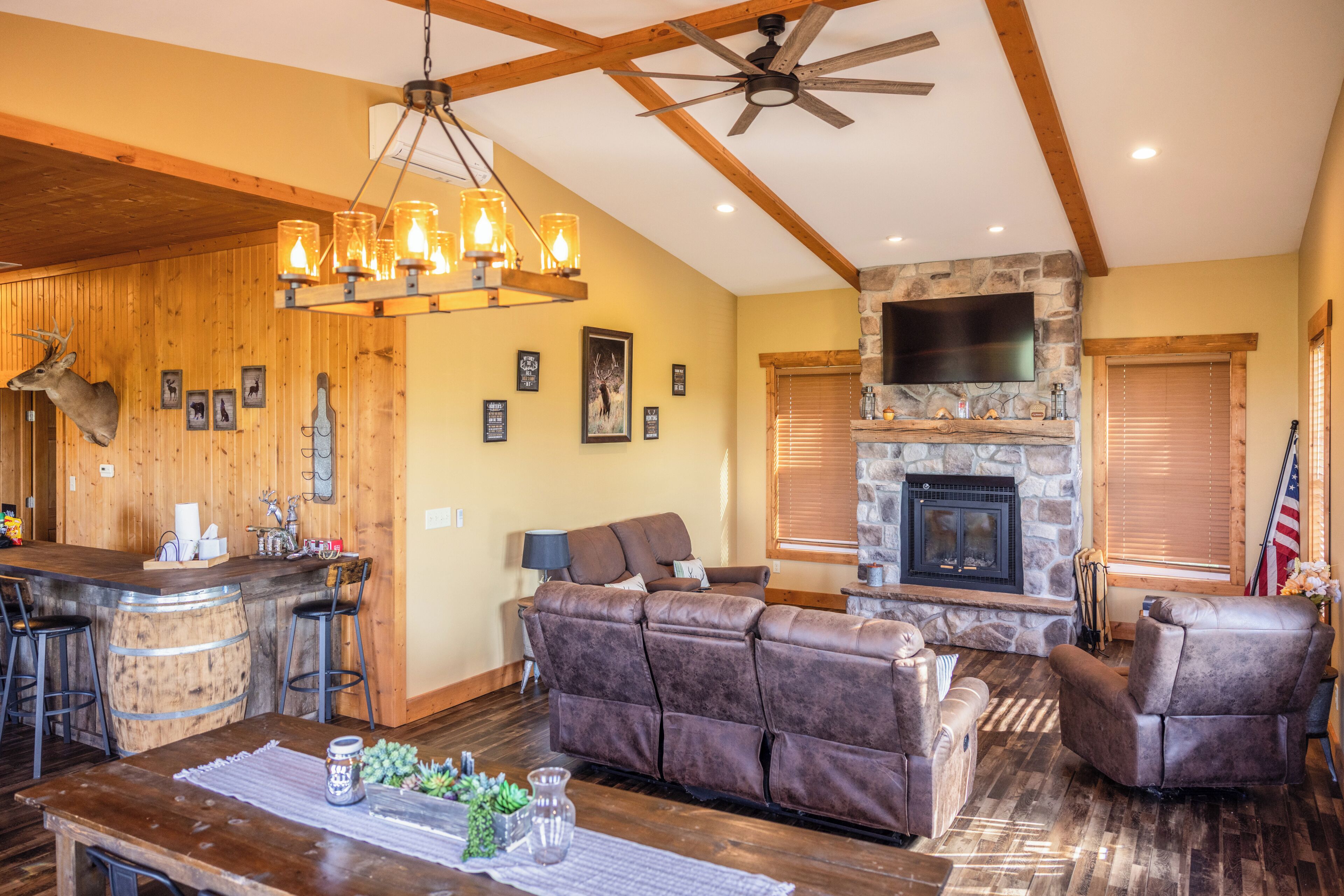 A rustic interior with a stone fireplace, wooden bar, leather sofas, and a ceiling fan.