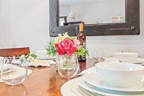 Ein Esszimmertisch ist gedeckt mit Tellern, Schüsseln, einer Weinflasche und einer Vase mit Blumen.