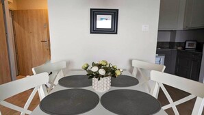 Een eethoek met een witte tafel, vier grijze placemats en een witte vaas met bloemen.