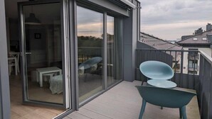 Een modern balkon met een glazen deur die leidt naar een binnenruimte, een houten terras en uitzicht op de stad.