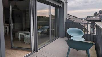 A modern balcony with a glass door leading to an interior space, a wooden deck, and a view of the cityscape.