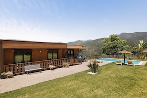 Una casa moderna con piscina, terraza de madera y vista a montañas.