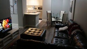 A living room with a TV, leather sofa, ottoman, and a dining area with chairs and a table.