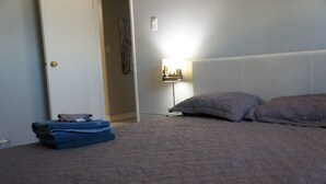 A bedroom with a bed, pillows, a folded blanket, a nightstand, and a wall-mounted lamp.