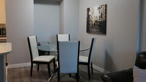 A dining area with a round table and four chairs, a black leather couch, and a framed picture on the wall.